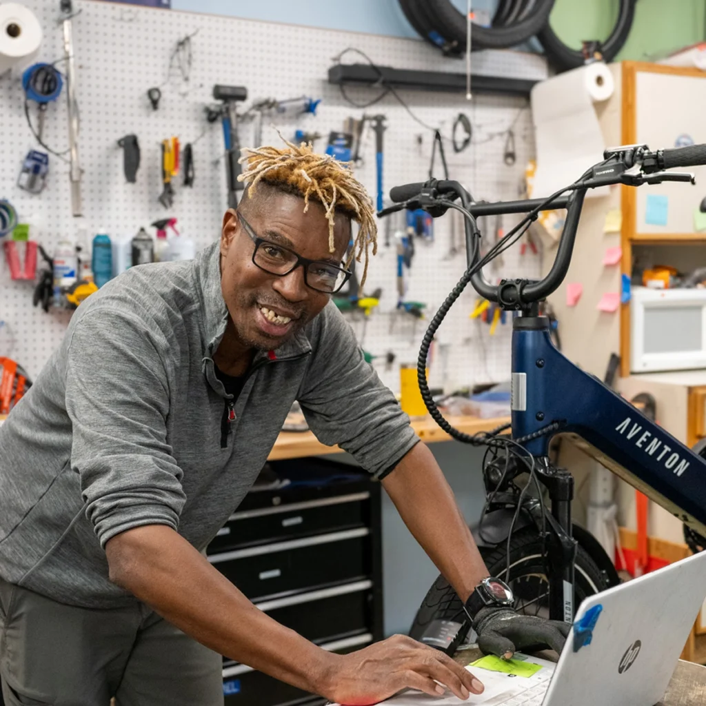 Friendly bike mechanic tunes Aventon e-bike with laptop in well-equipped workshop.