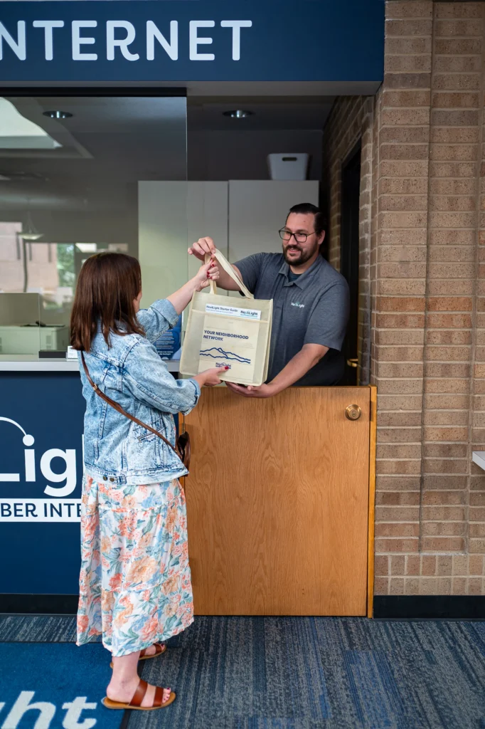 Customer picks up fiber internet starter kit at service window from smiling staffer.