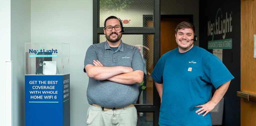 NextLight service center staff by Whole Home WiFi display, smiling in office lobby, customer support.