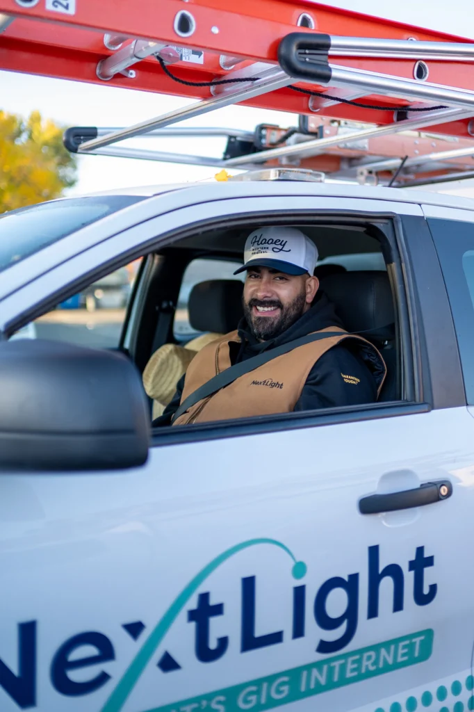 Technician ready to set up NextLight U4 U6 WiFi router, smiling from a branded fiber gig internet service truck with a roof ladder.