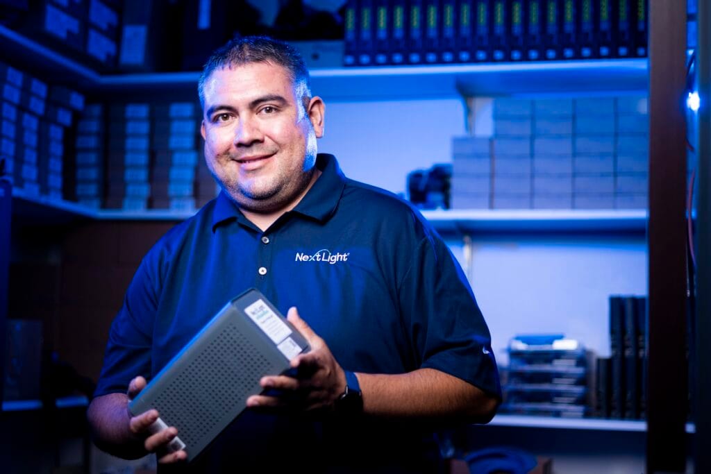 NextLight WiFi router setup U4 U6 with a smiling internet technician holding networking hardware in an organized tech storeroom.